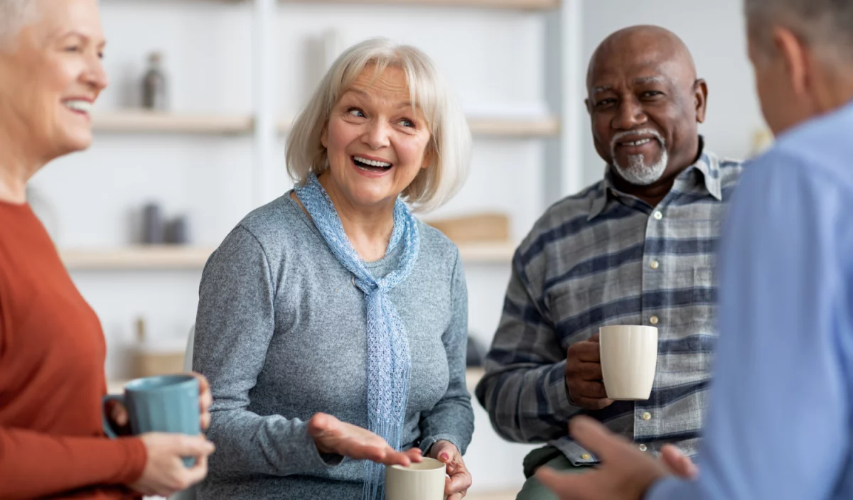 Des résidents du Jardin des sages discutent autour d’un café, souriants, dans une ambiance conviviale.