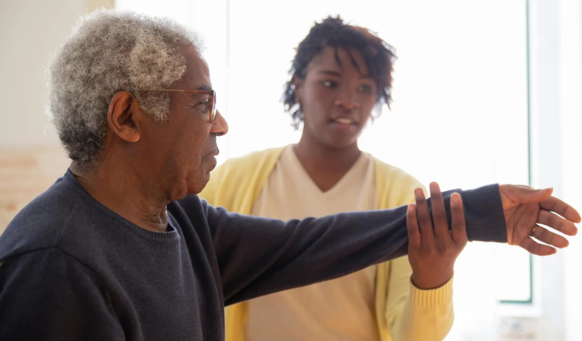 Une ergothérapeute accompagne un résident dans ses exercices de mobilité au Jardin des sages.
