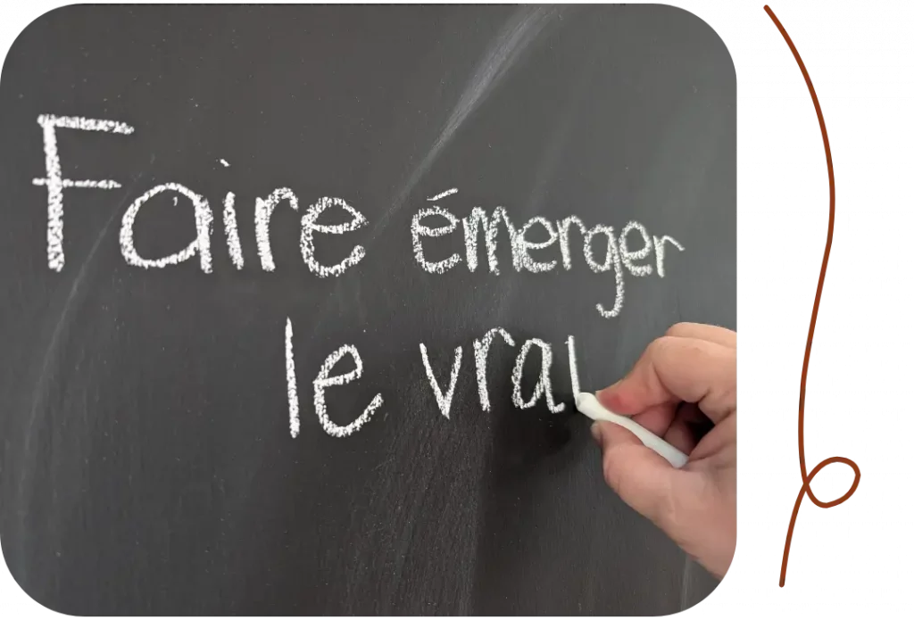 Main écrivant l'expression « Faire émerger le vrai » sur un tableau noir.