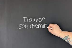 Main écrivant « Trouver son chemin » sur un tableau noir illustrant la réflexion stratégique en communication.